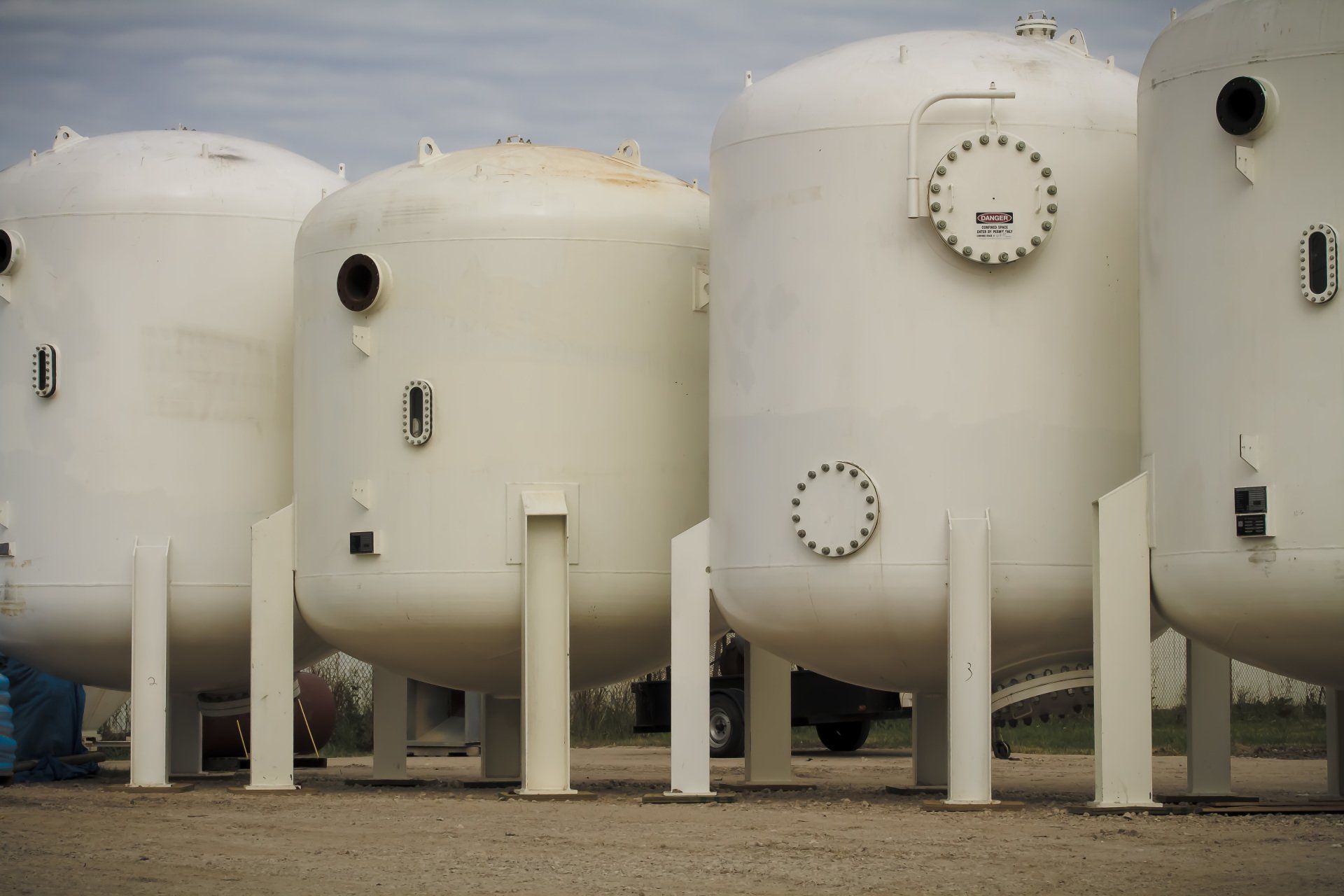 A row of white tanks are lined up in a field.