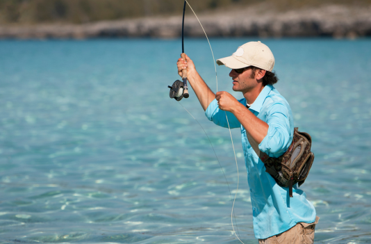 A man in a blue shirt is fishing in the ocean