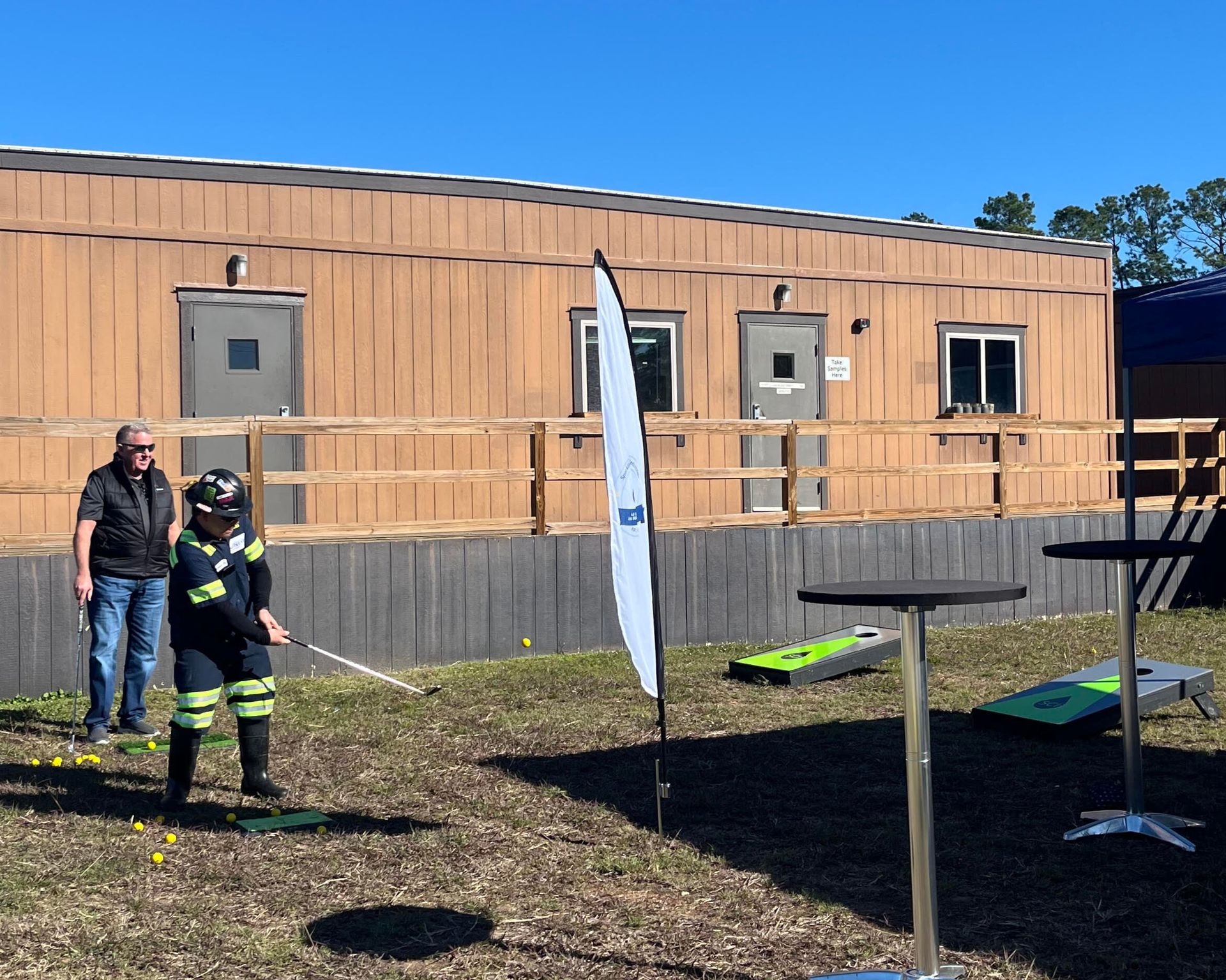 People in work attire gather outdoors near a tent and a building. Some are wearing hard hats.