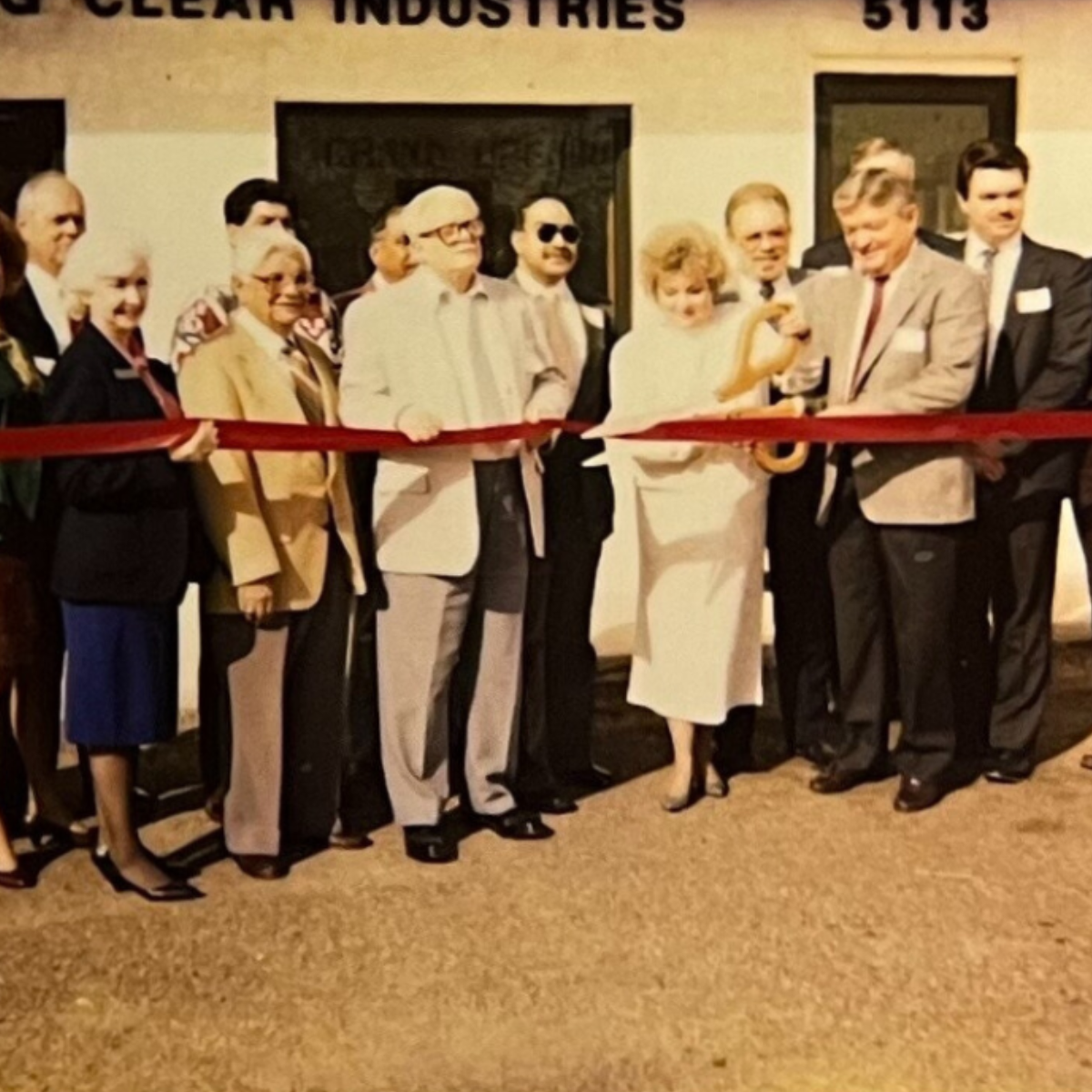 A group of people cutting a red ribbon in front of a building that says Sparkling Clear Industries