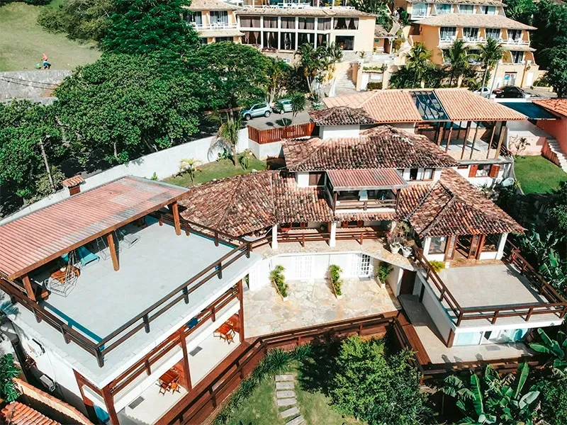 Vista aérea de vários edifícios com telhados de telha vermelha e detalhes em madeira, rodeados por vegetação.