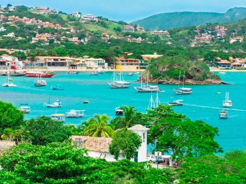 Baía vibrante de cor turquesa com barcos, vegetação verdejante e casas nas colinas sob um céu azul.
