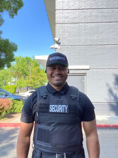 A man wearing a security vest and hat is standing in front of a building.