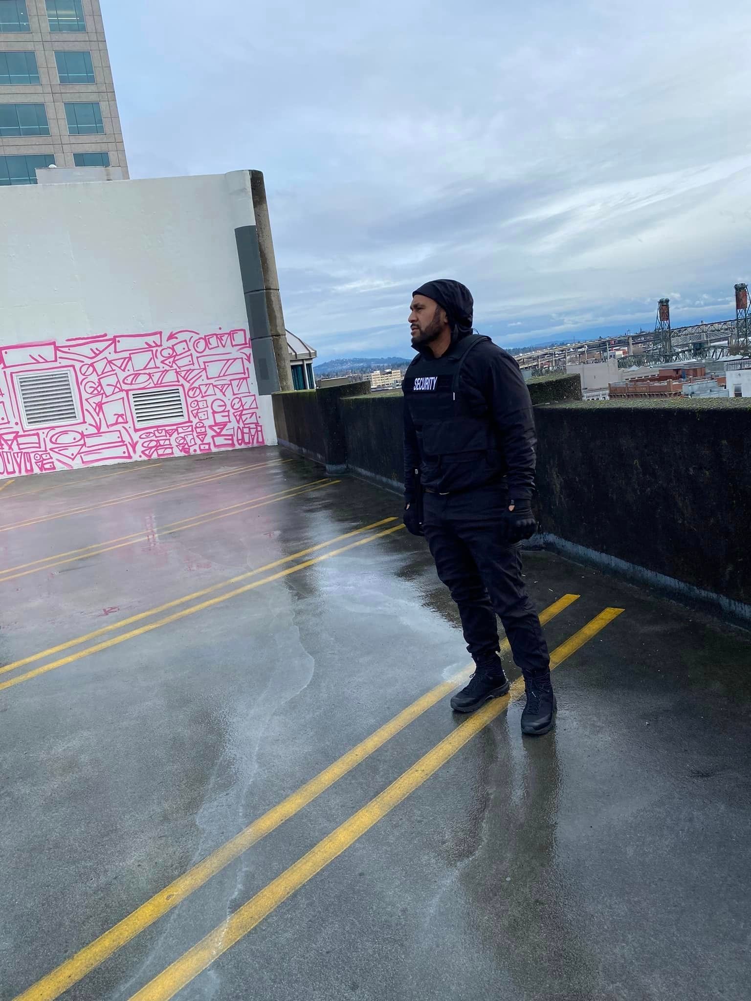 A man in a black hoodie is standing in the rain on a wet street.