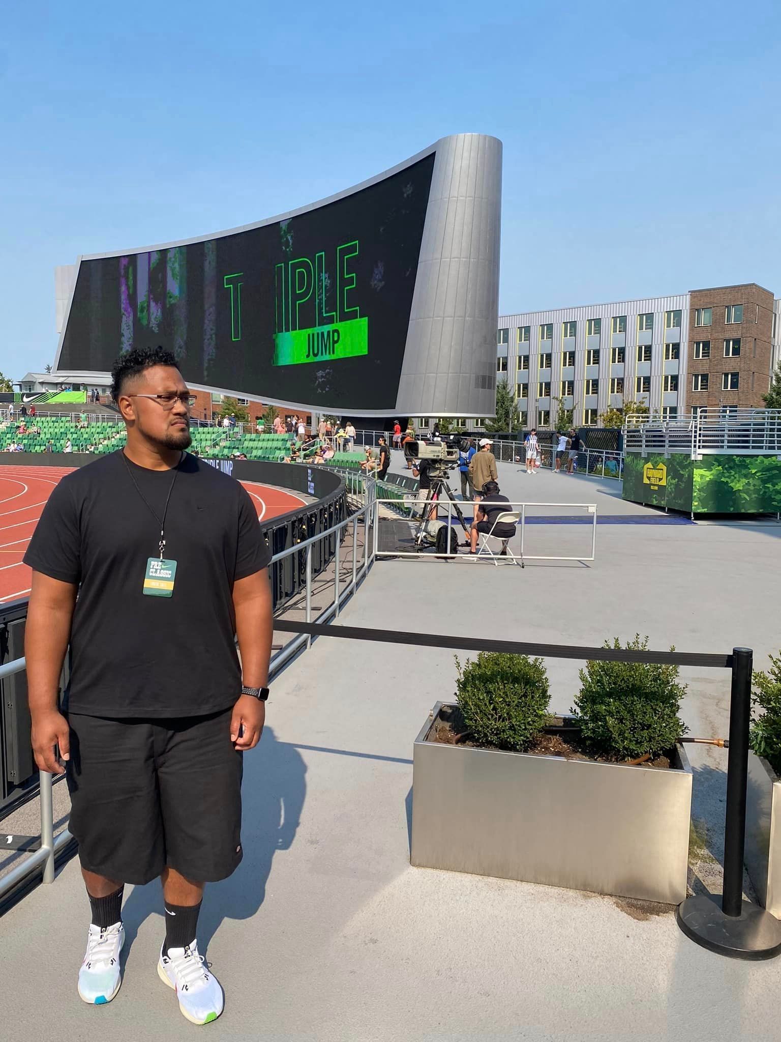 A man in a black shirt and shorts is standing in front of a large screen.