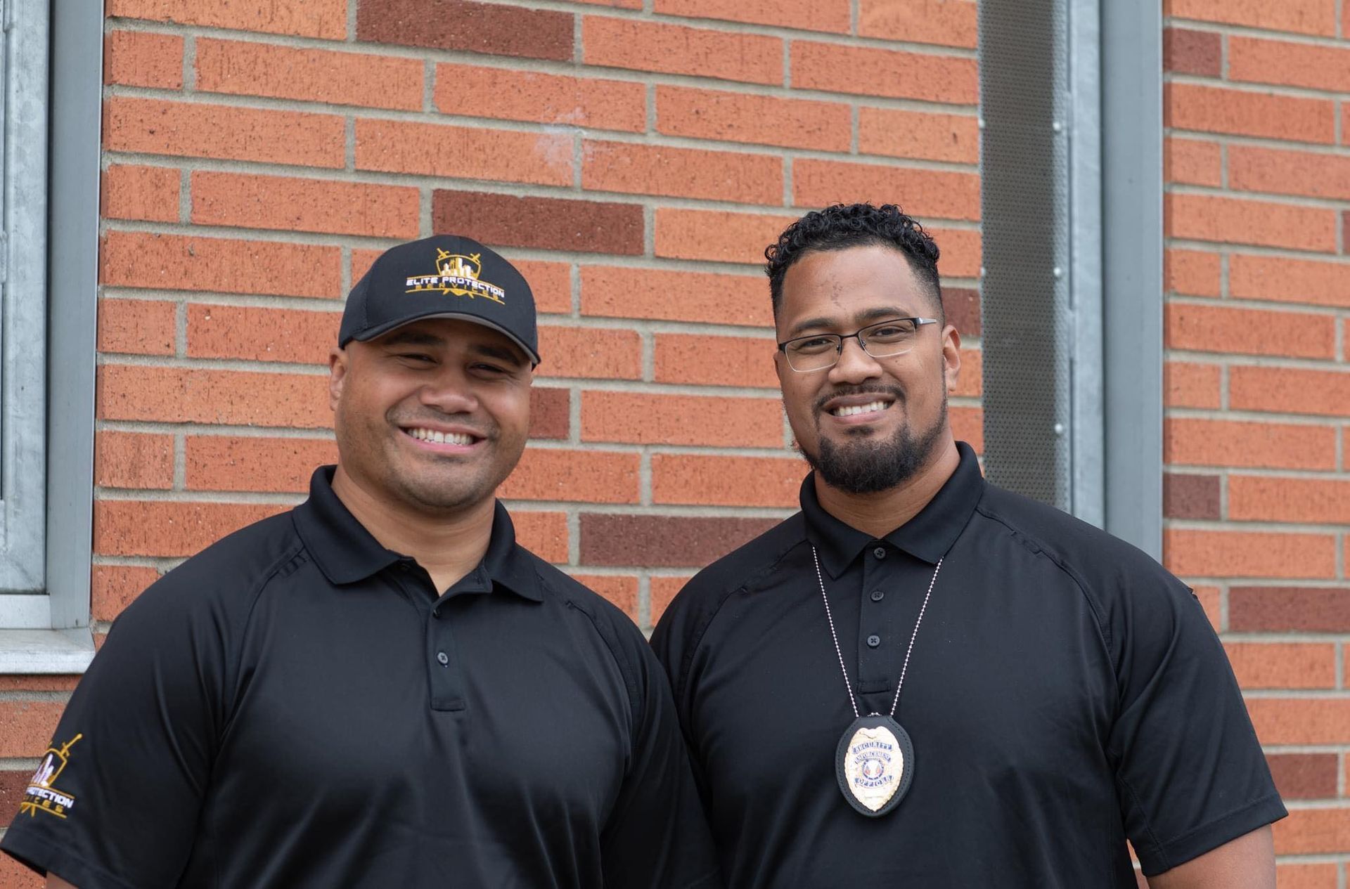 Two men are standing next to each other in front of a brick wall.