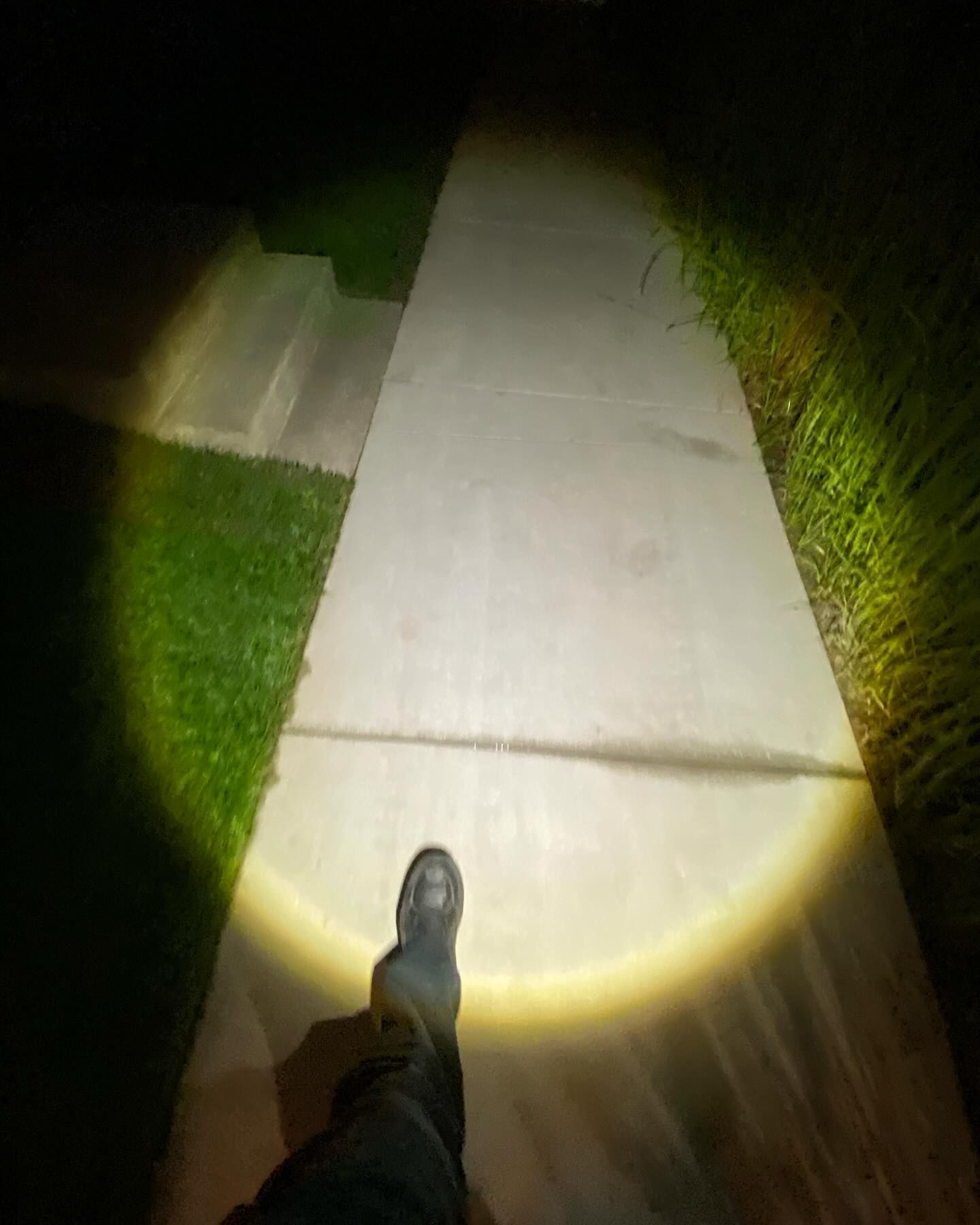 A person is walking down a sidewalk at night with a flashlight shining on them.