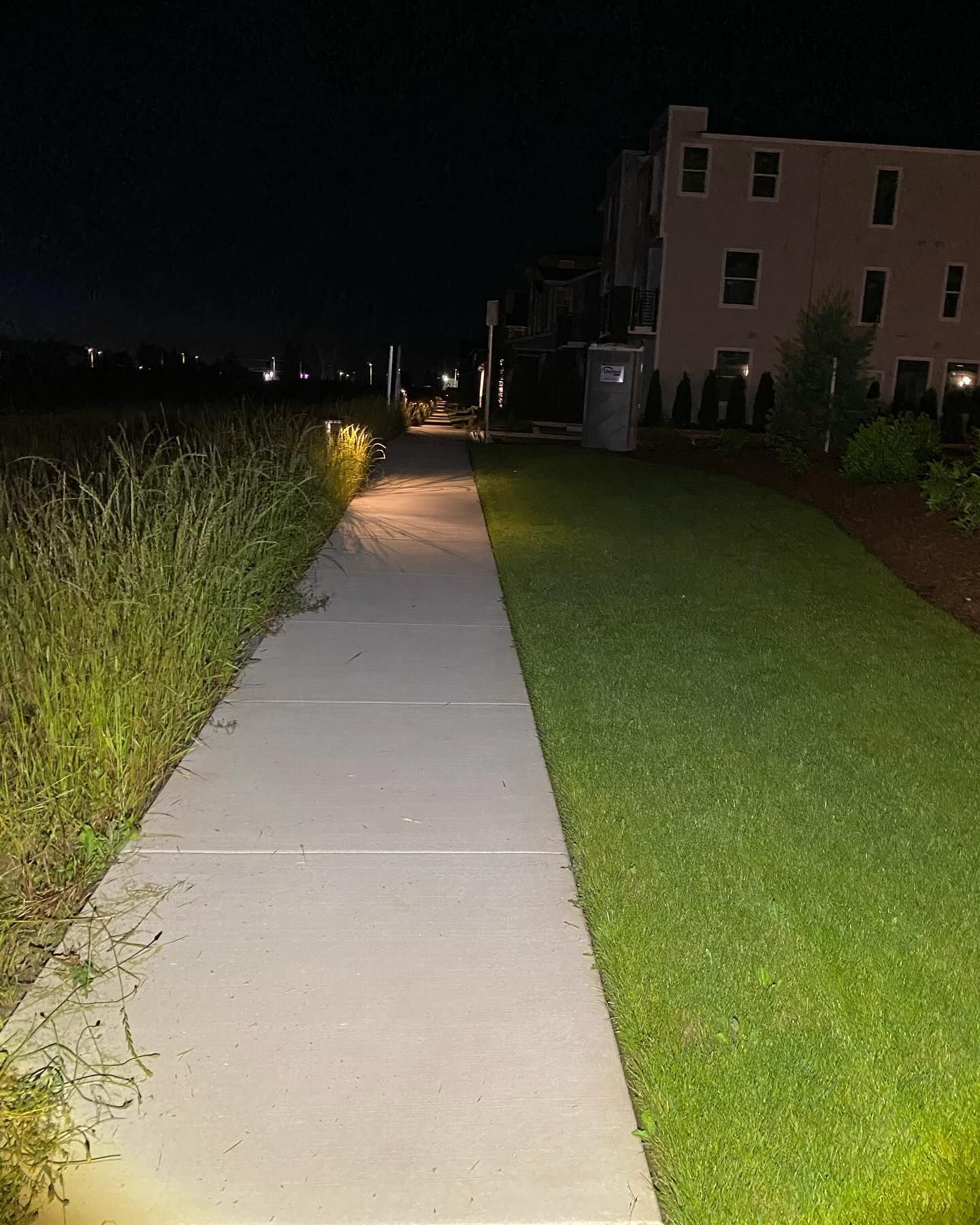A sidewalk is lit up at night with a building in the background.