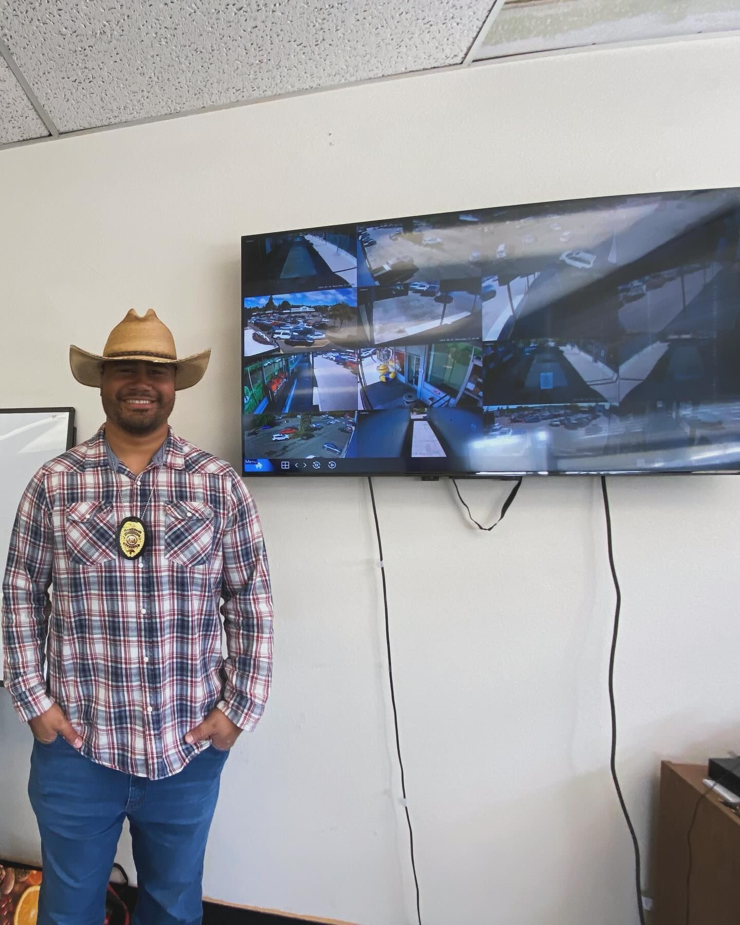 A man wearing a cowboy hat is standing in front of a flat screen tv