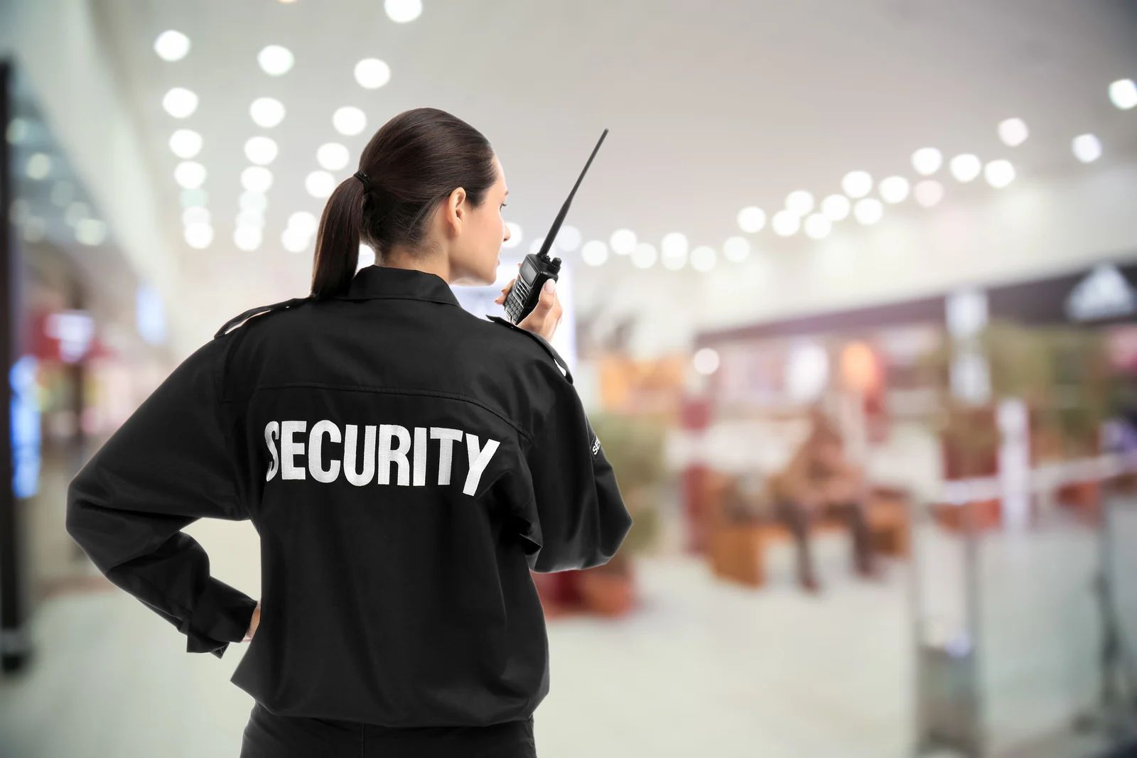 Security guard with radio standing in a blurred shopping mall corridor, seen from behind