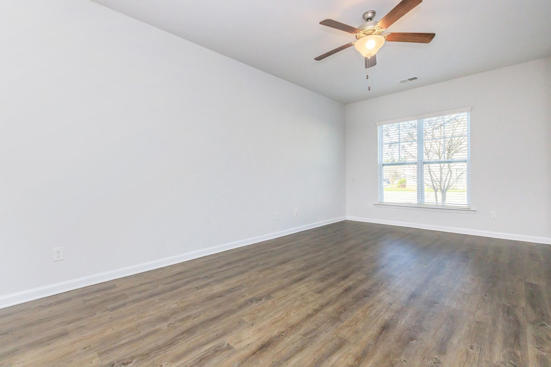 An empty living room with hardwood floors and a ceiling fan.