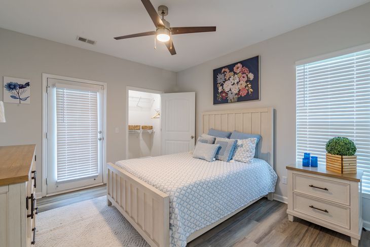 Patio with table and chairs, overlooking apartments. Green bushes and fence line the edge.