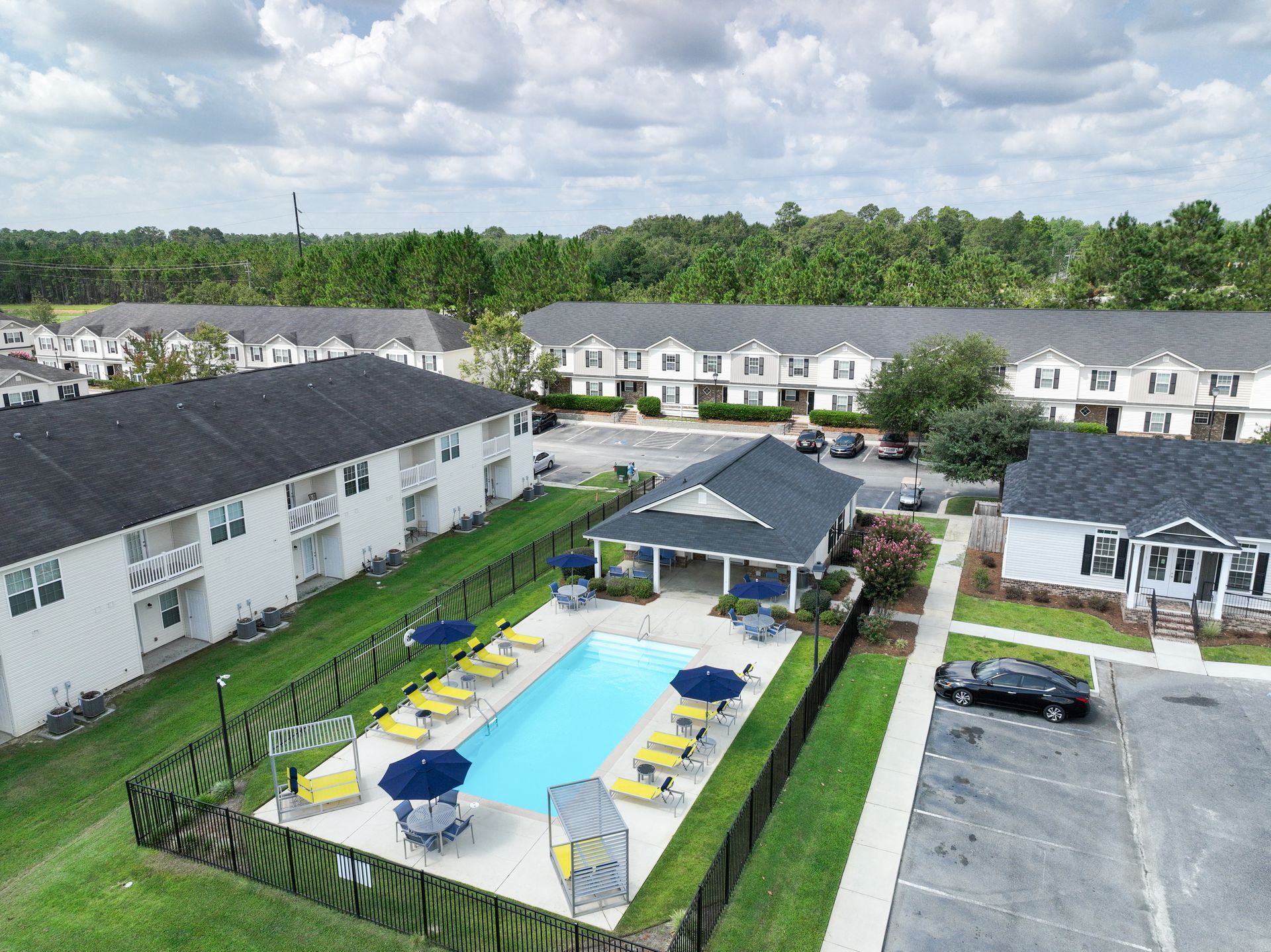 Poolside area with black metal table/chairs, lounge chairs, and building under blue sky.