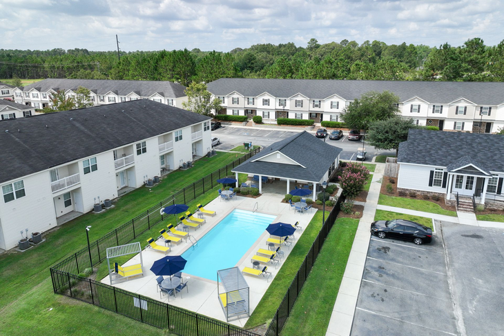 Poolside area with black metal table/chairs, lounge chairs, and building under blue sky.