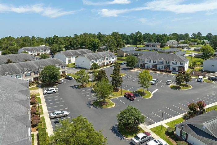 Aerial view of an apartment complex with parking lot and trees under a blue sky.