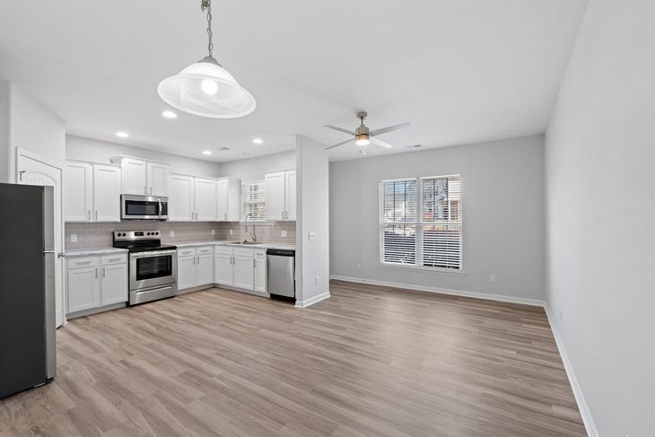 Modern kitchen with white cabinets, stainless steel appliances, and light wood floors.