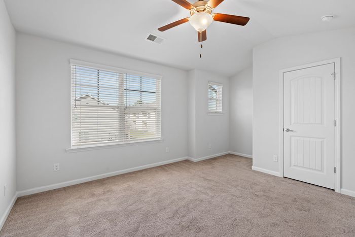 Empty bedroom with beige carpet, white walls, and a ceiling fan. Includes a window with blinds and a closed door.