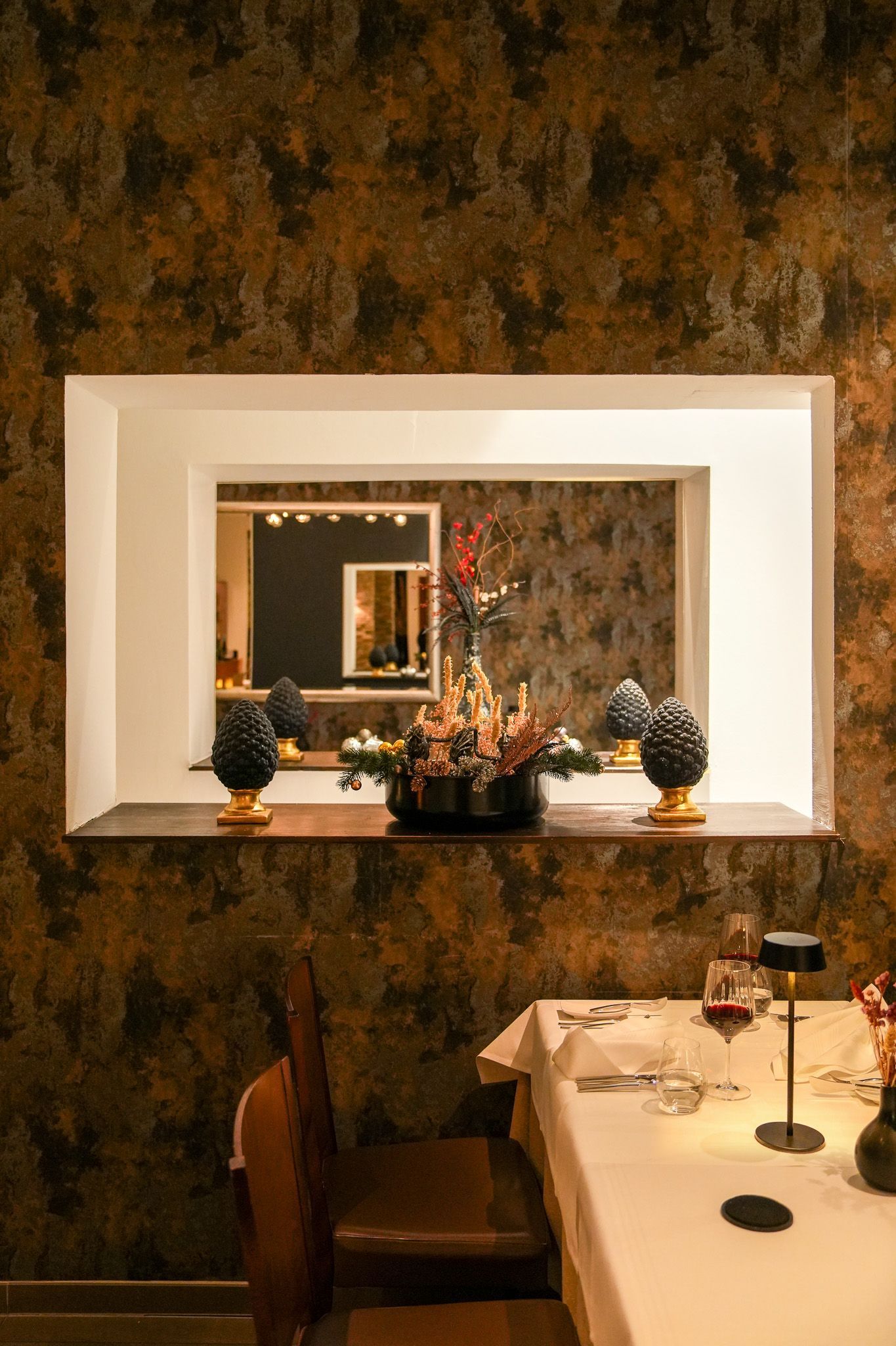 Esszimmer mit Blumenarrangement auf einem Regal in einer Wandnische. Braune, strukturierte Wände, gedeckter Tisch.