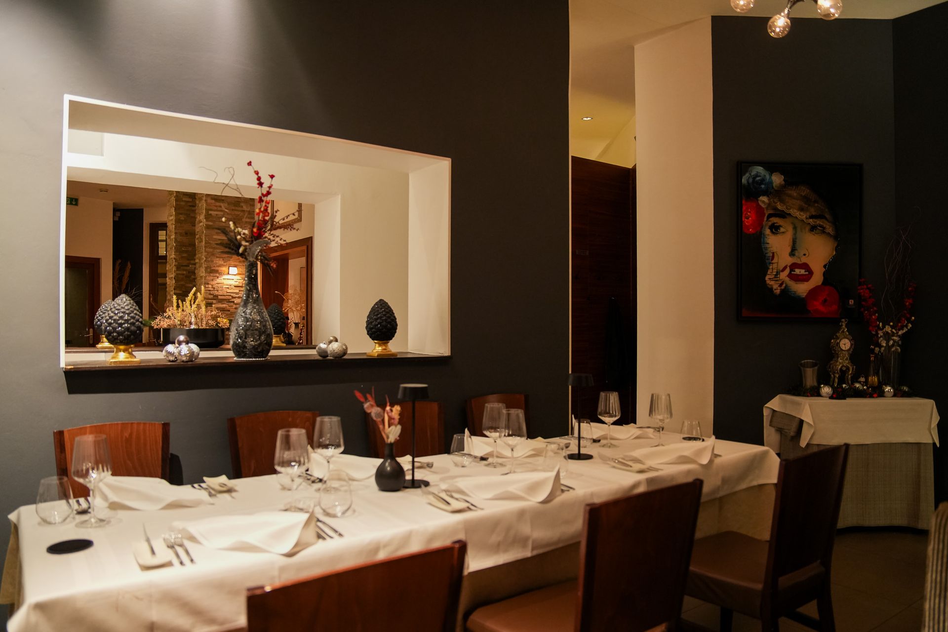 Ein formell gedeckter Esstisch in einem Restaurant mit dunkelgrauen Wänden, einem Spiegel und Kunstwerken.