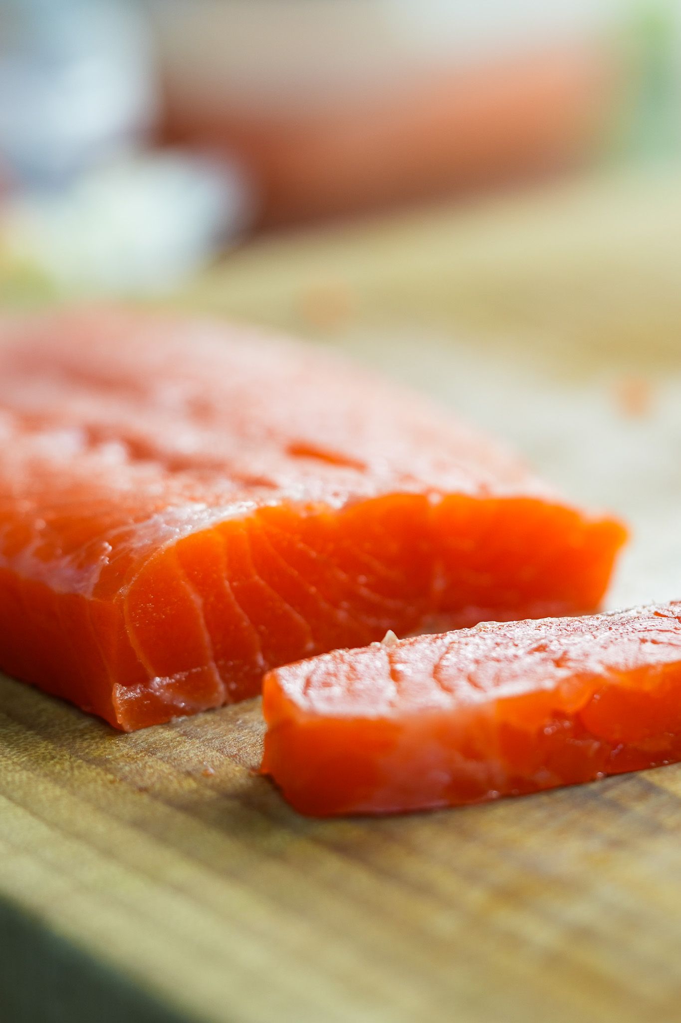 Rohes Lachsfilet auf einem Holzbrett, von dem eine Scheibe abgeschnitten ist.