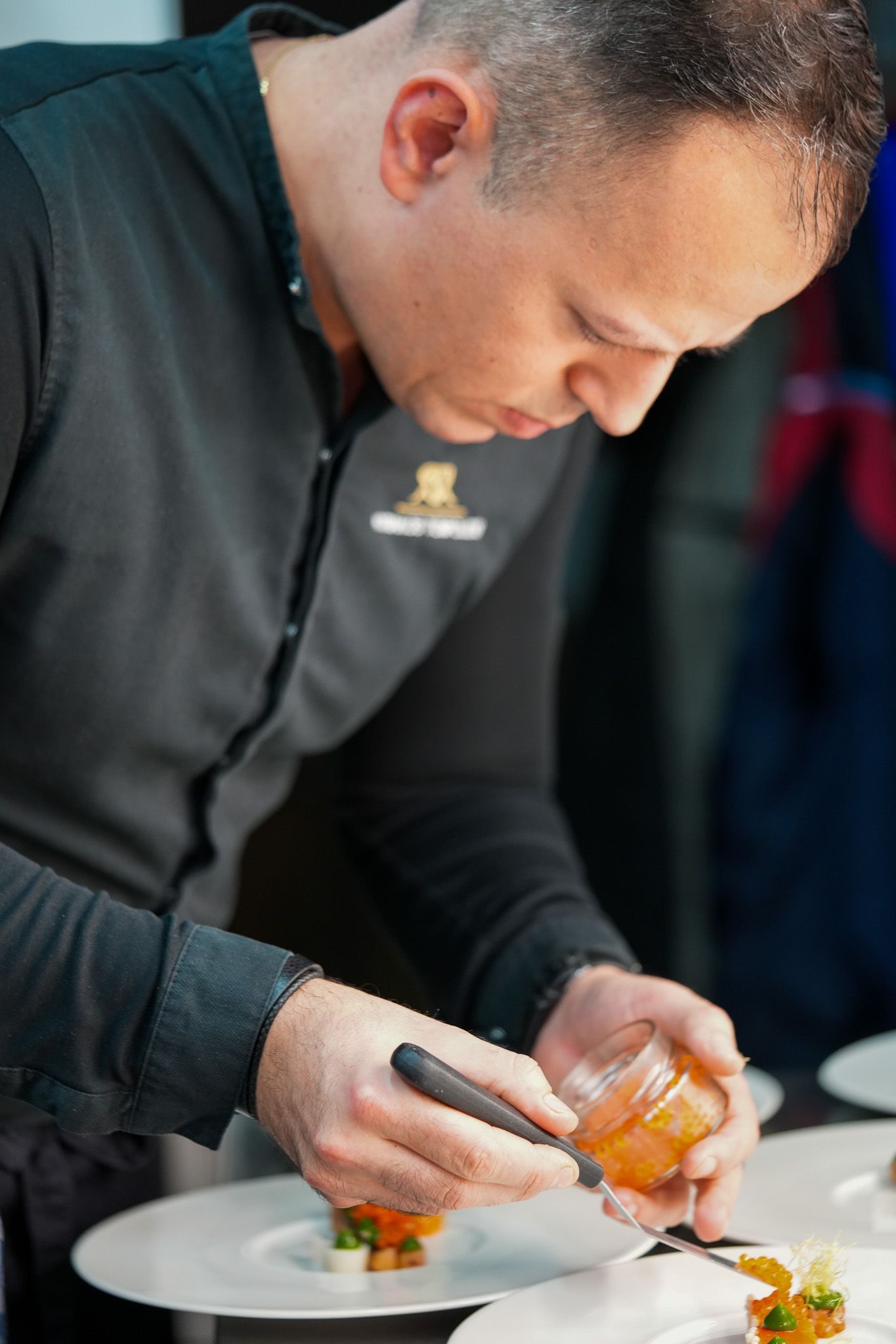 Ein Koch garniert in einem Restaurant, bekleidet mit einem schwarzen Hemd, sorgfältig Teller mit Kaviar.
