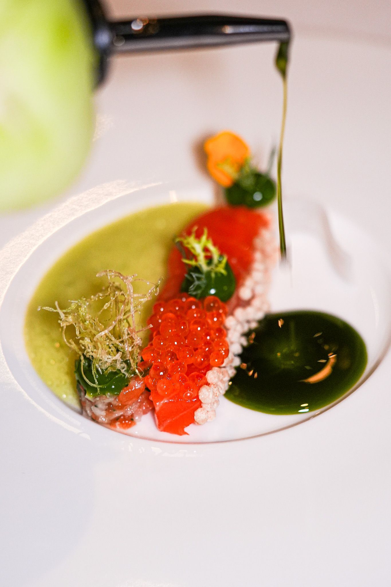 Gourmetgericht mit Lachskaviar, grüner Sauce und Garnitur, beträufelt mit Öl.
