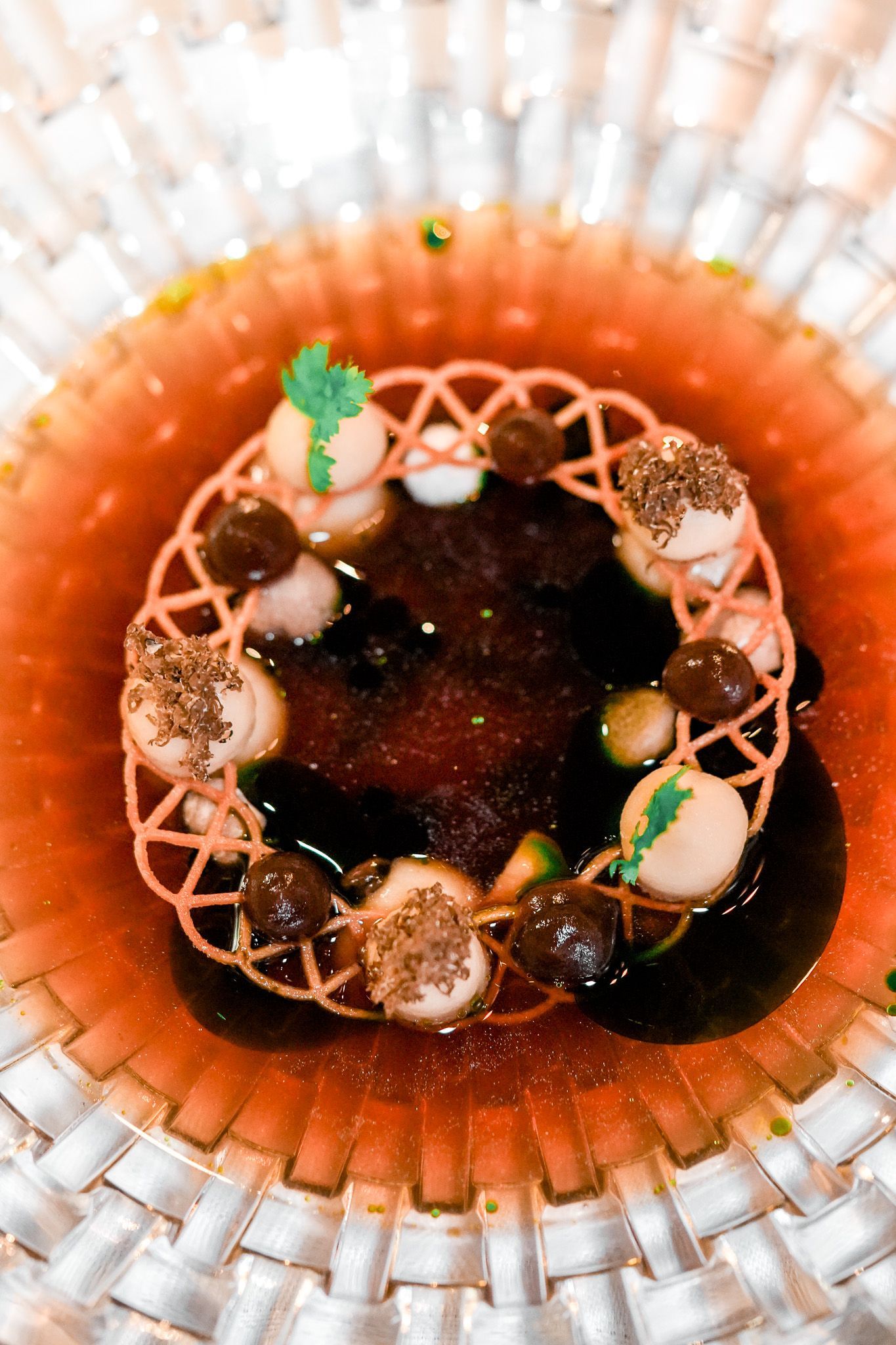 Ein rosa Gitter umgibt dunkle Flüssigkeit, kleine Kugeln in einer durchsichtigen Schale.