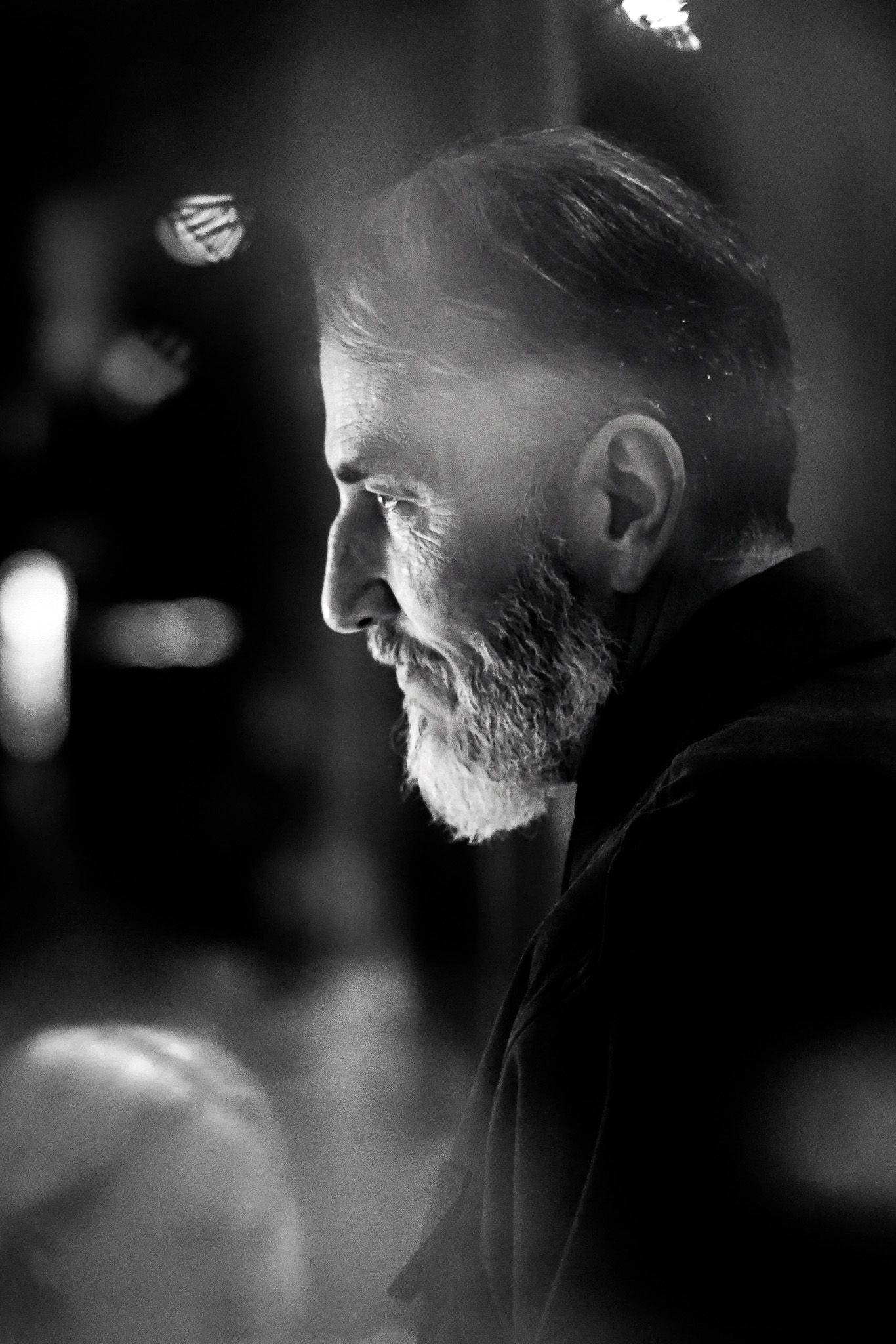 Mann mit Bart im Profil, beleuchtet von einer unsichtbaren Lichtquelle. Schwarz-Weiß-Fotografie, unscharfer Hintergrund.