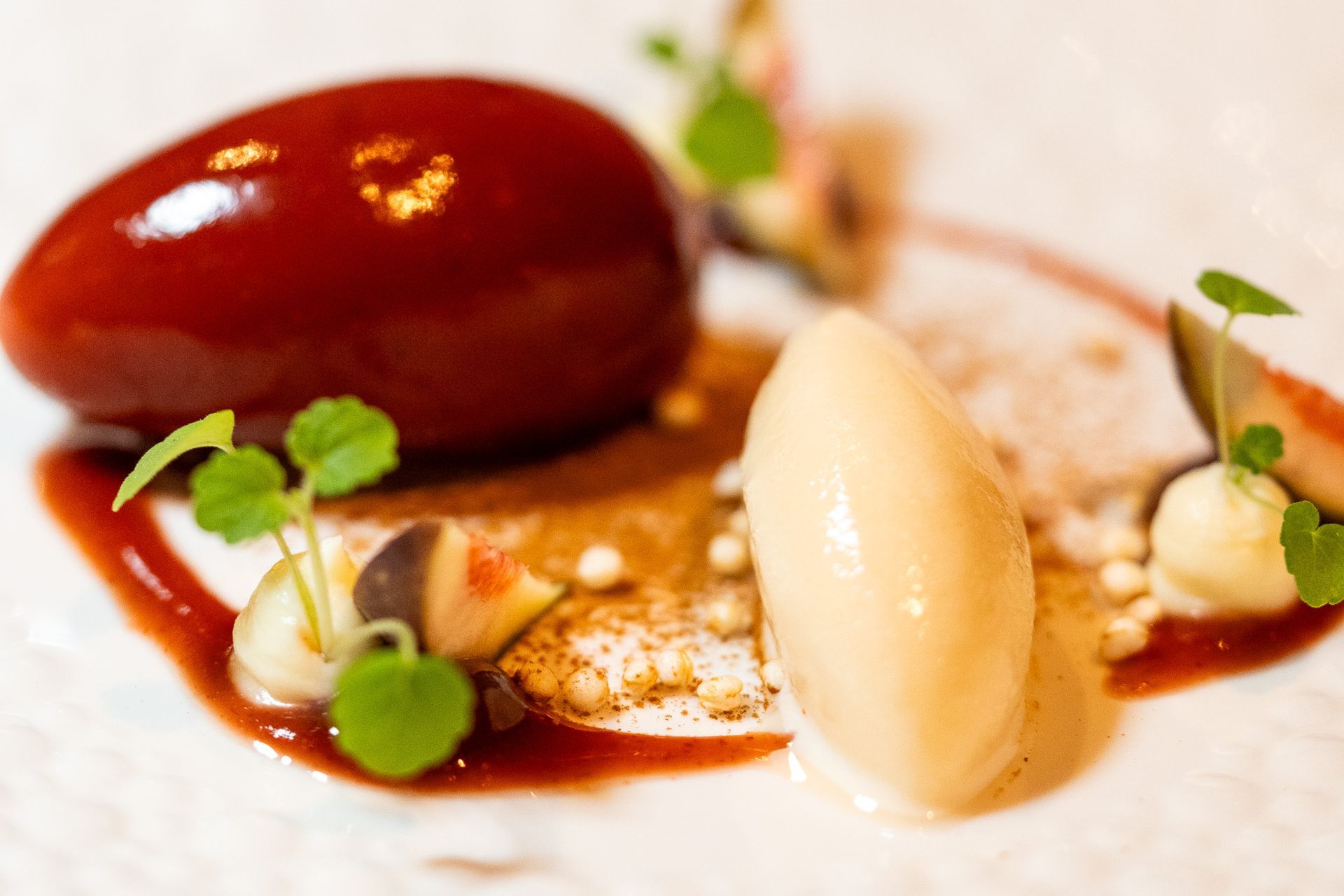 Gourmet-Dessert: glänzend rote Kugel, helle Kugel, Sauce, Feigen, Microgreens auf einem weißen Teller.
