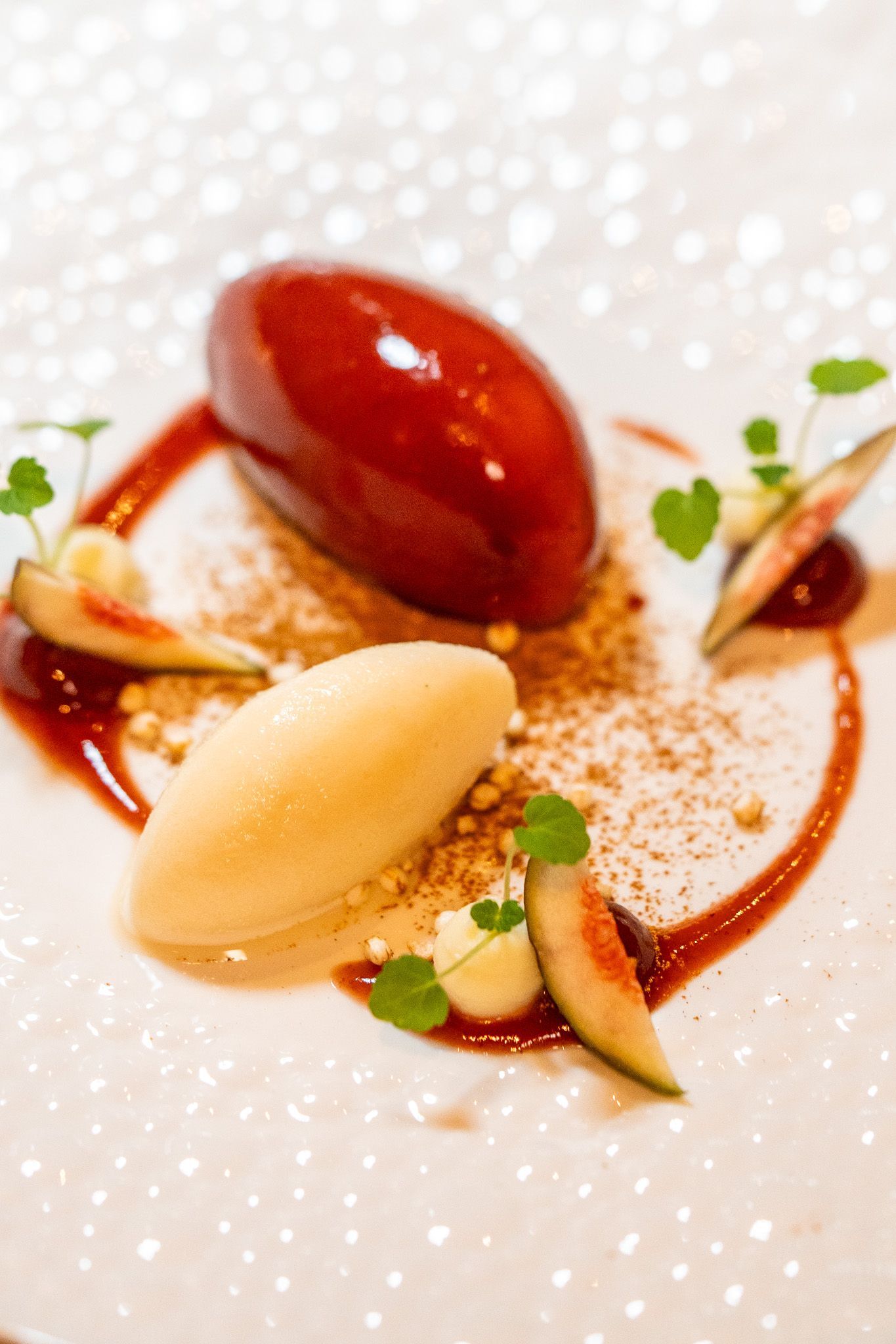 Dessertteller mit einem rot glasierten Gebäck, einer gelben Kugel Eis, Feigen und Sauce.