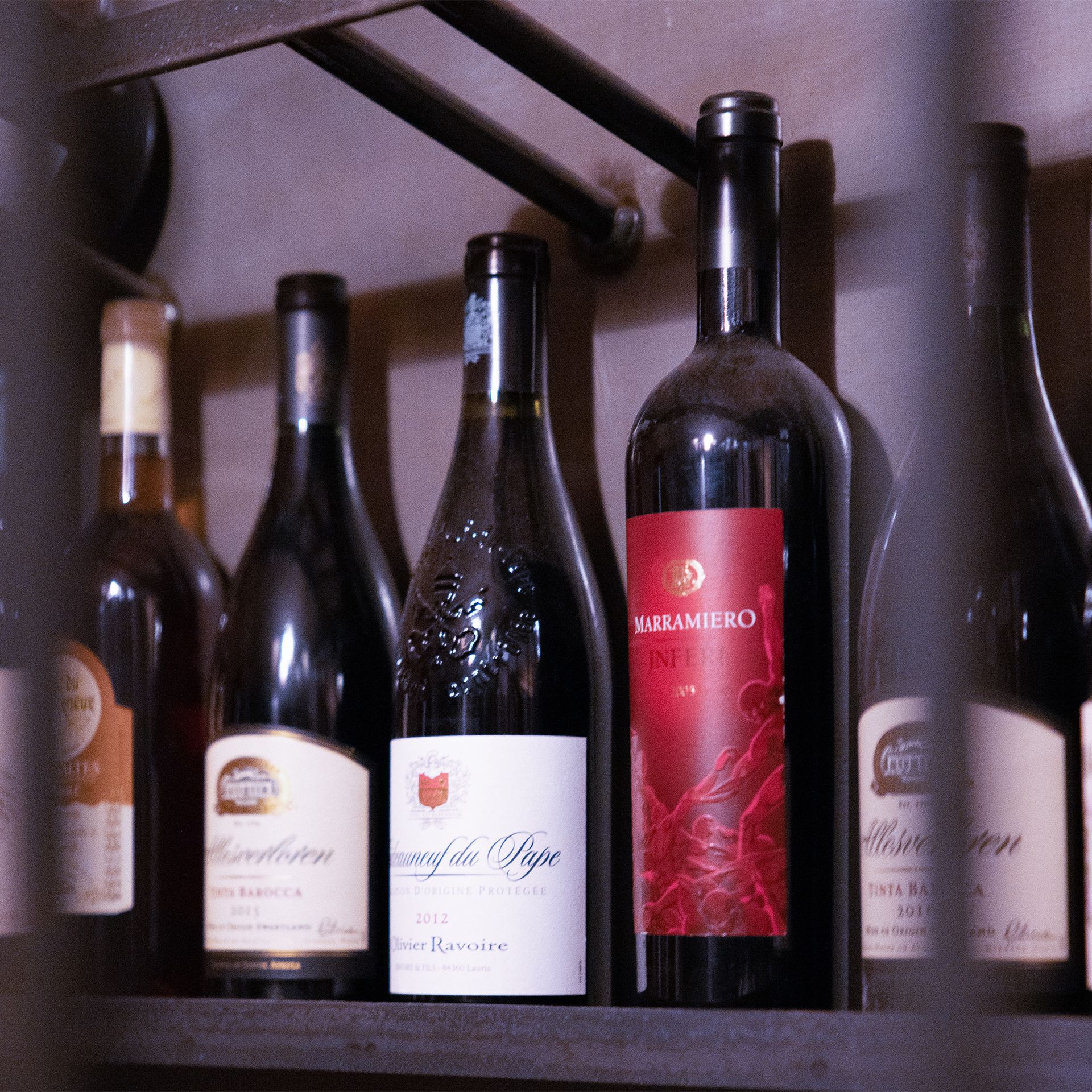 Weinflaschen in verschiedenen Formen und Größen auf einem Regal, mit Etiketten in unterschiedlichen Farben.