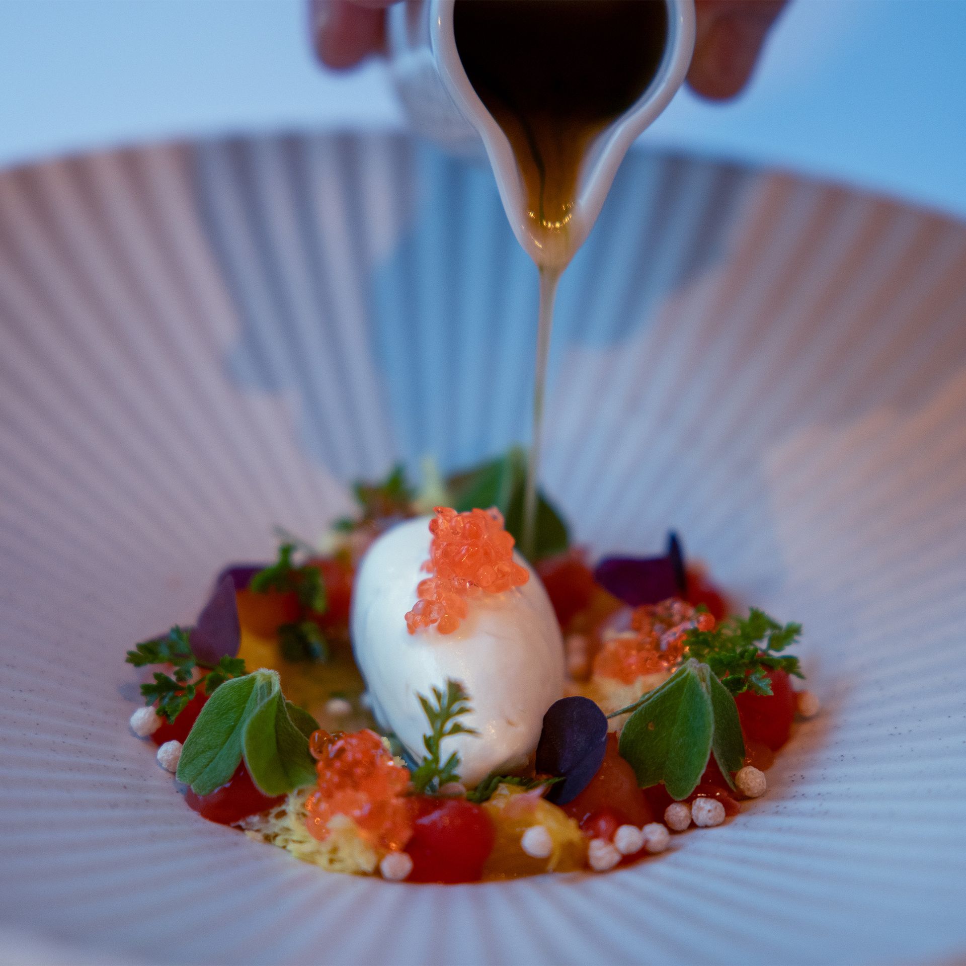Dessertteller mit weißem Eis, rotem Kaviar und Sauce, die darüber gegossen wird.