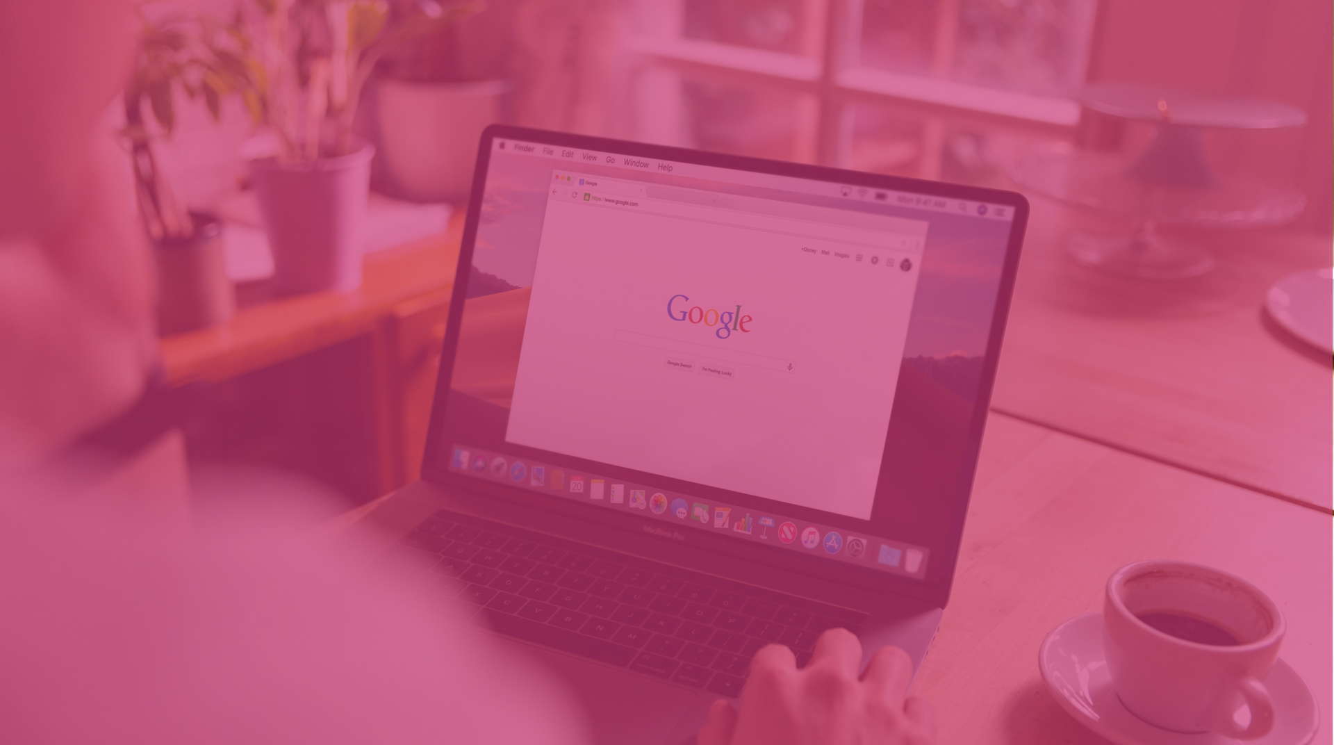 Person using a laptop at a desk with a coffee cup in a pink-tinted room