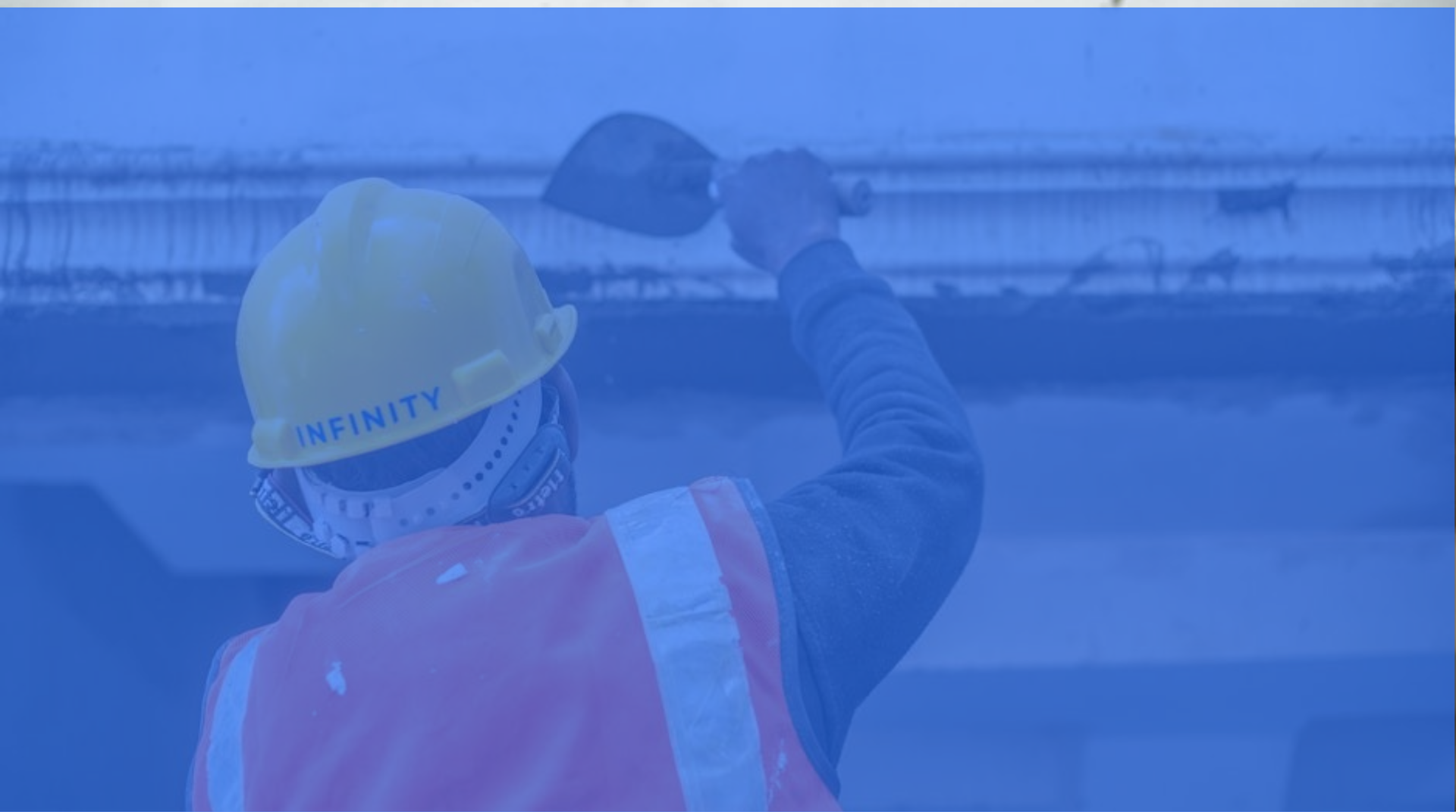 Worker in yellow hard hat and orange vest inspecting a bridge or industrial structure over water