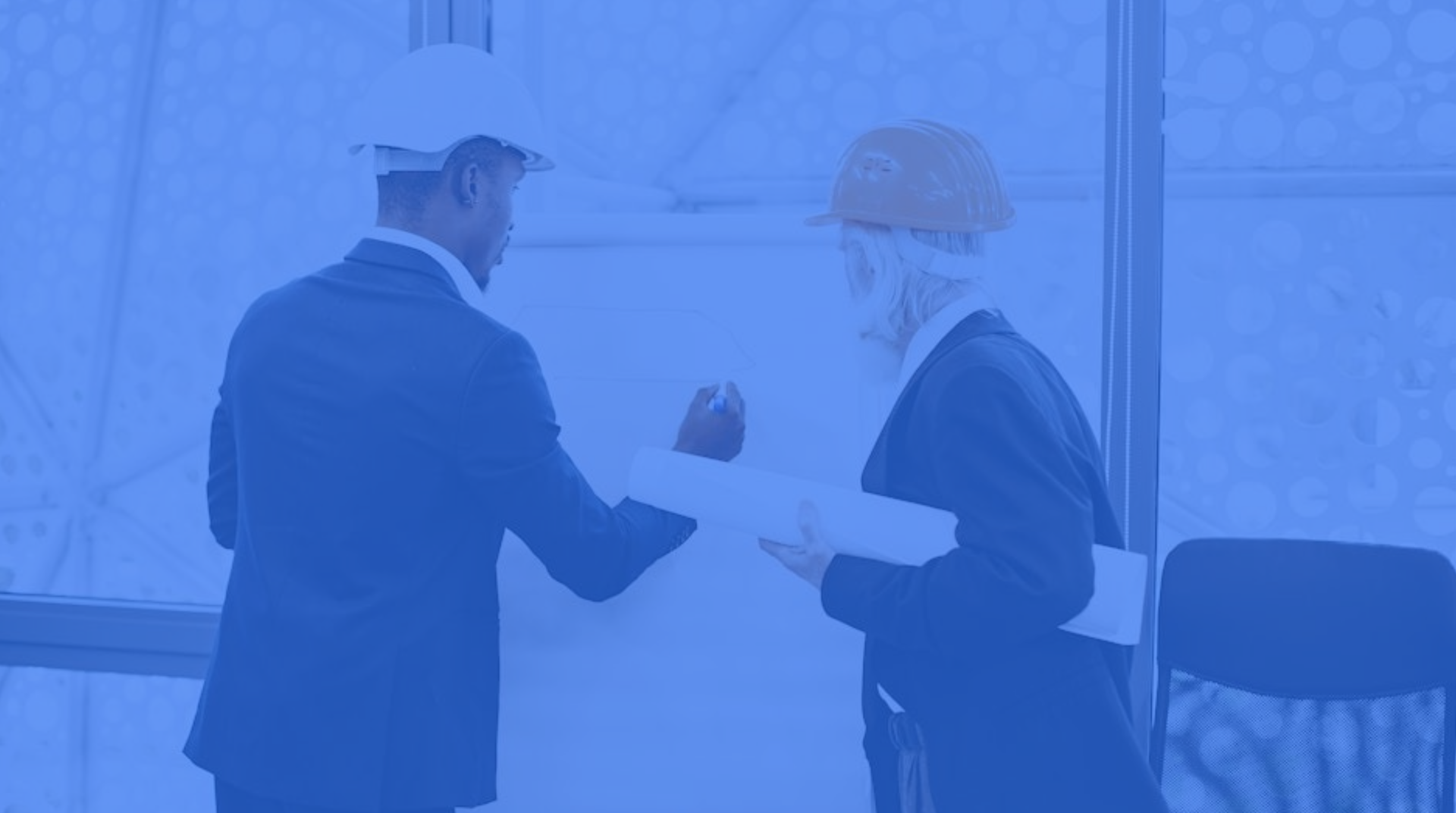 Two coworkers in hard hats exchanging papers at a construction site, blue-tinted scene