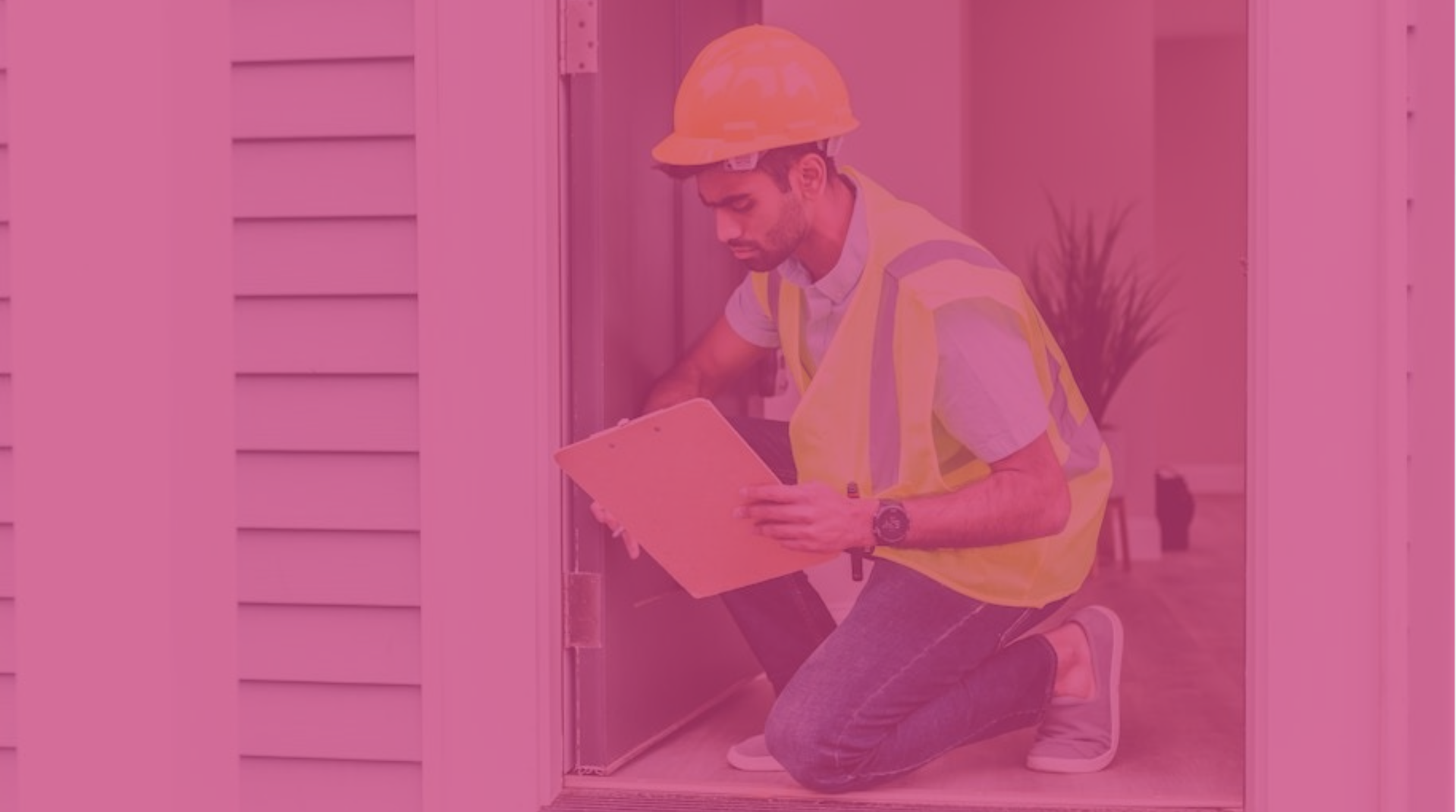 Contractor crouching at residential construction site checking clipboard