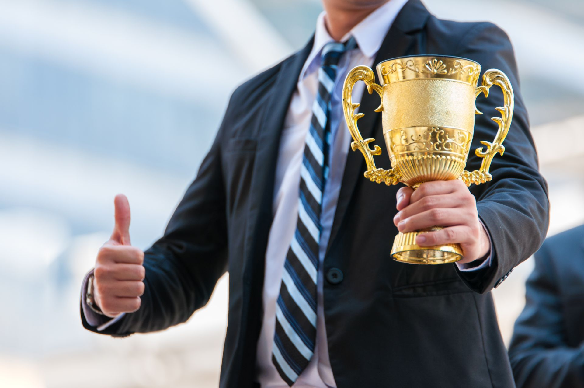 A man in a suit and tie is holding a trophy and giving a thumbs up.