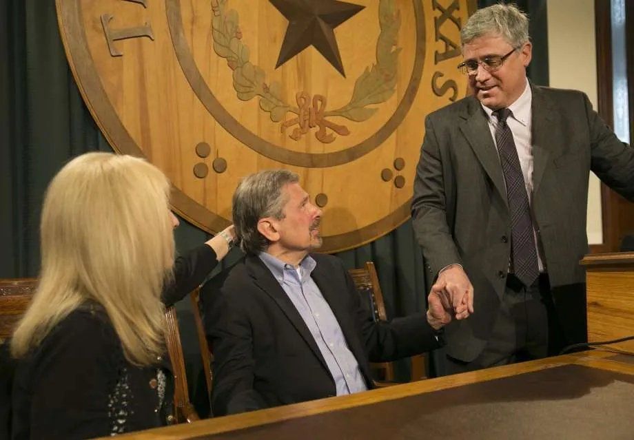 A group of people are sitting at a table in front of a texas seal.