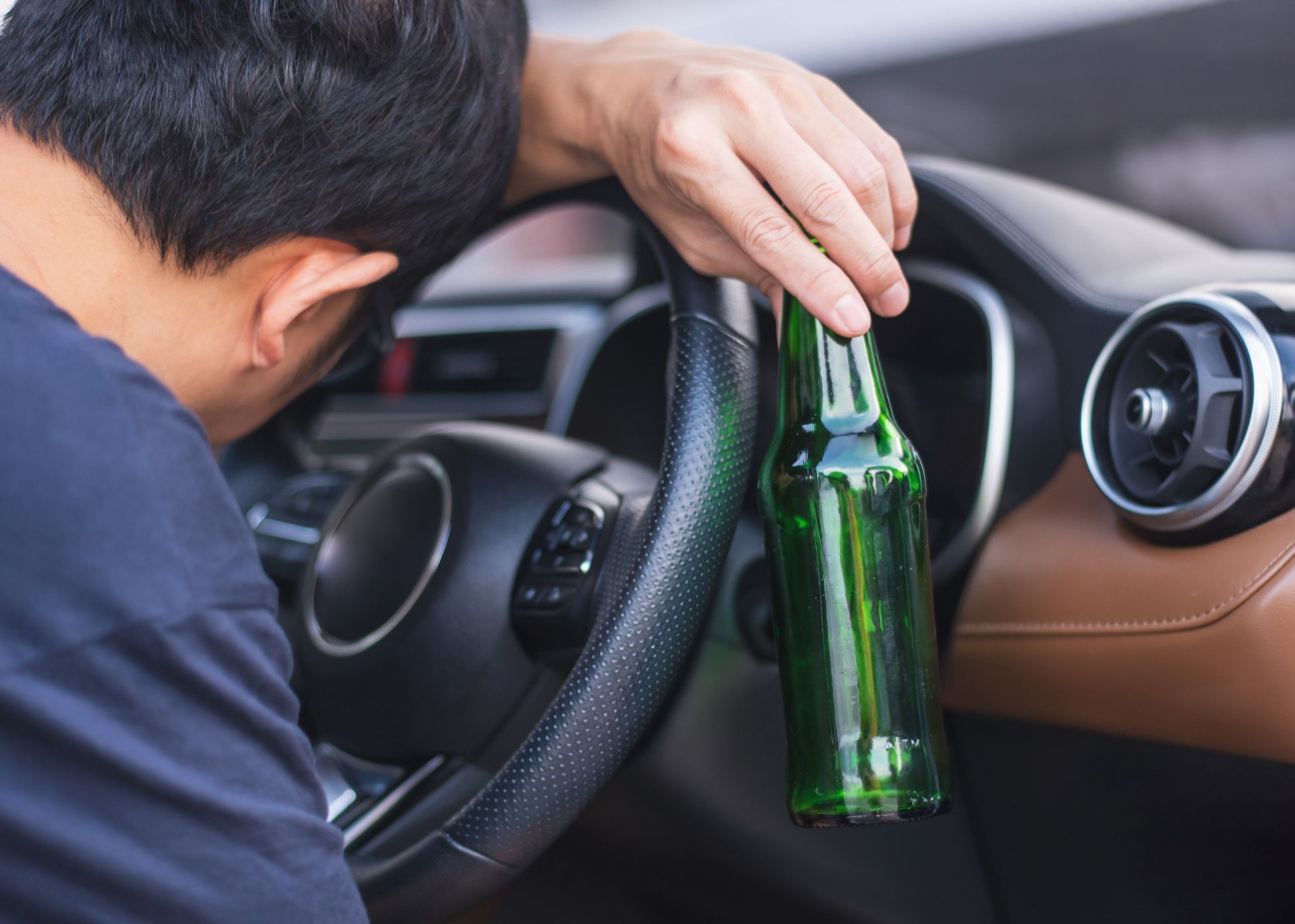 A man is sitting in a car holding a bottle of beer.