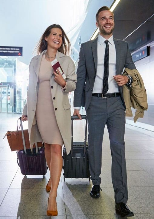 A man and a woman are walking through an airport with their luggage.