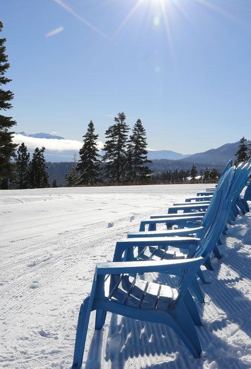 A row of blue chairs in the snow with mountains in the background