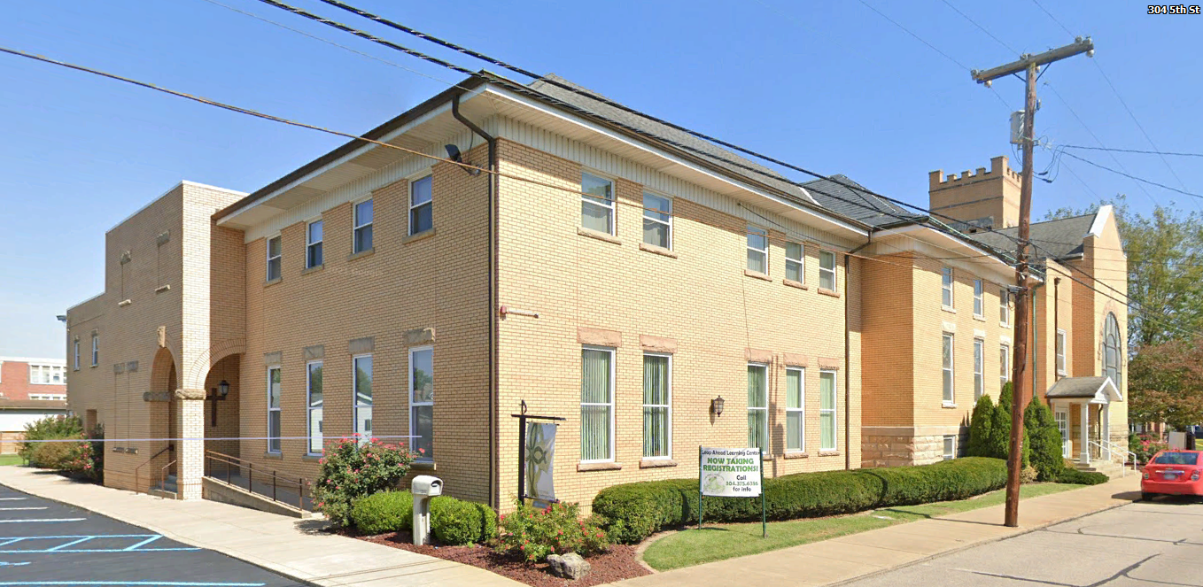 A large yellow building with a lot of windows is sitting on the corner of a street.