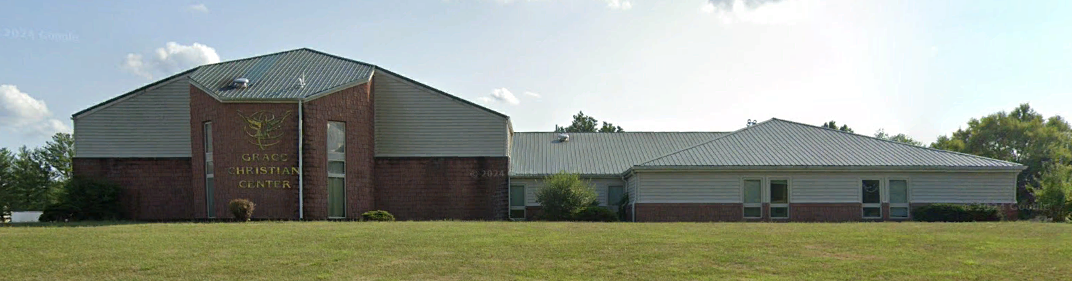 A large brick building with a white roof is in the middle of a grassy field.