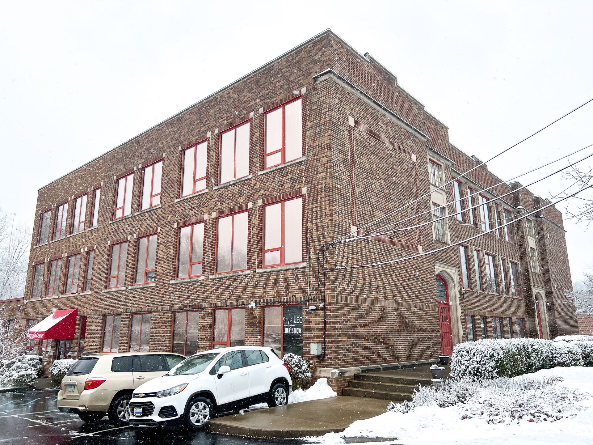 A brick building with cars parked in front of it in the snow.