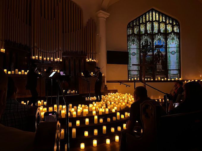 A group of people are sitting in a church surrounded by candles.