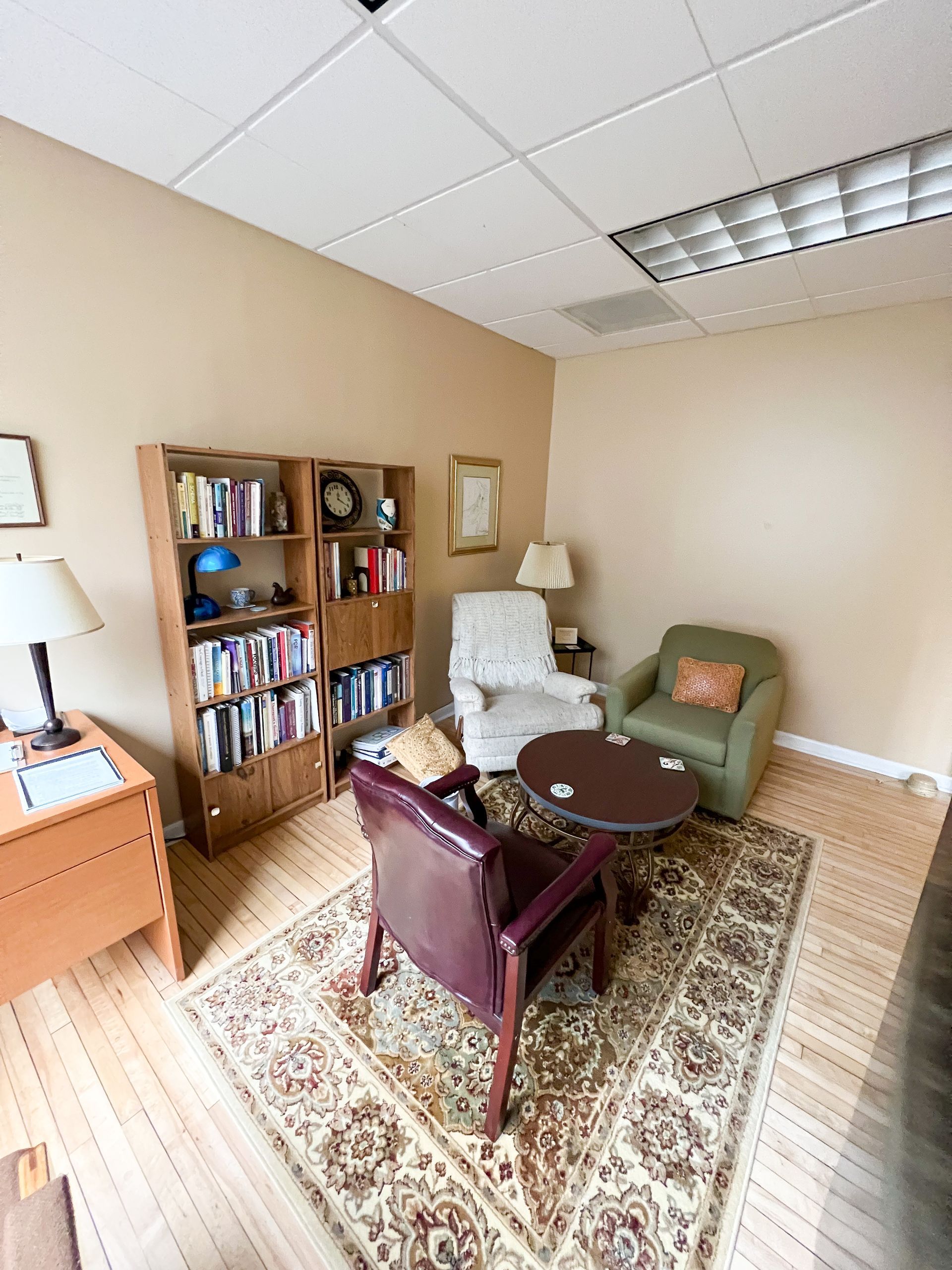 A living room with chairs , a table , a bookshelf and a rug.