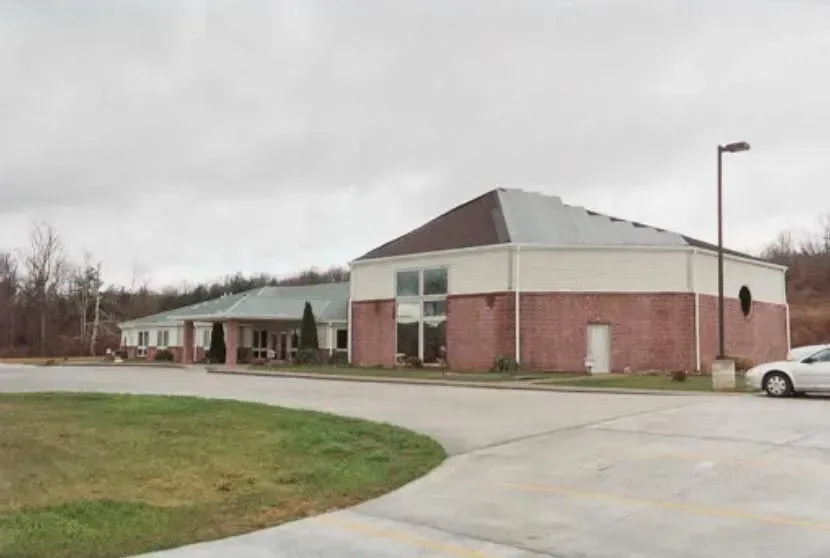 A white car is parked in front of a large brick building.