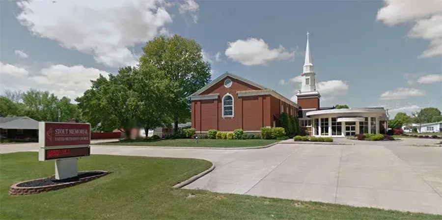 A church with a steeple and a sign in front of it.