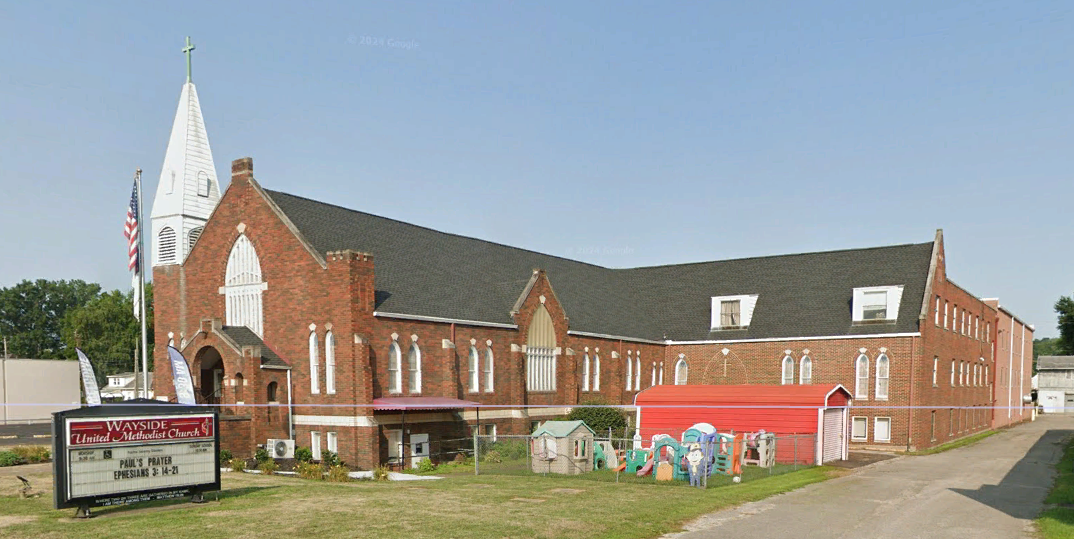 A large brick church with a steeple and a sign in front of it.