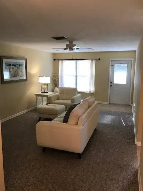 A living room with a couch , chair , ottoman and a ceiling fan.